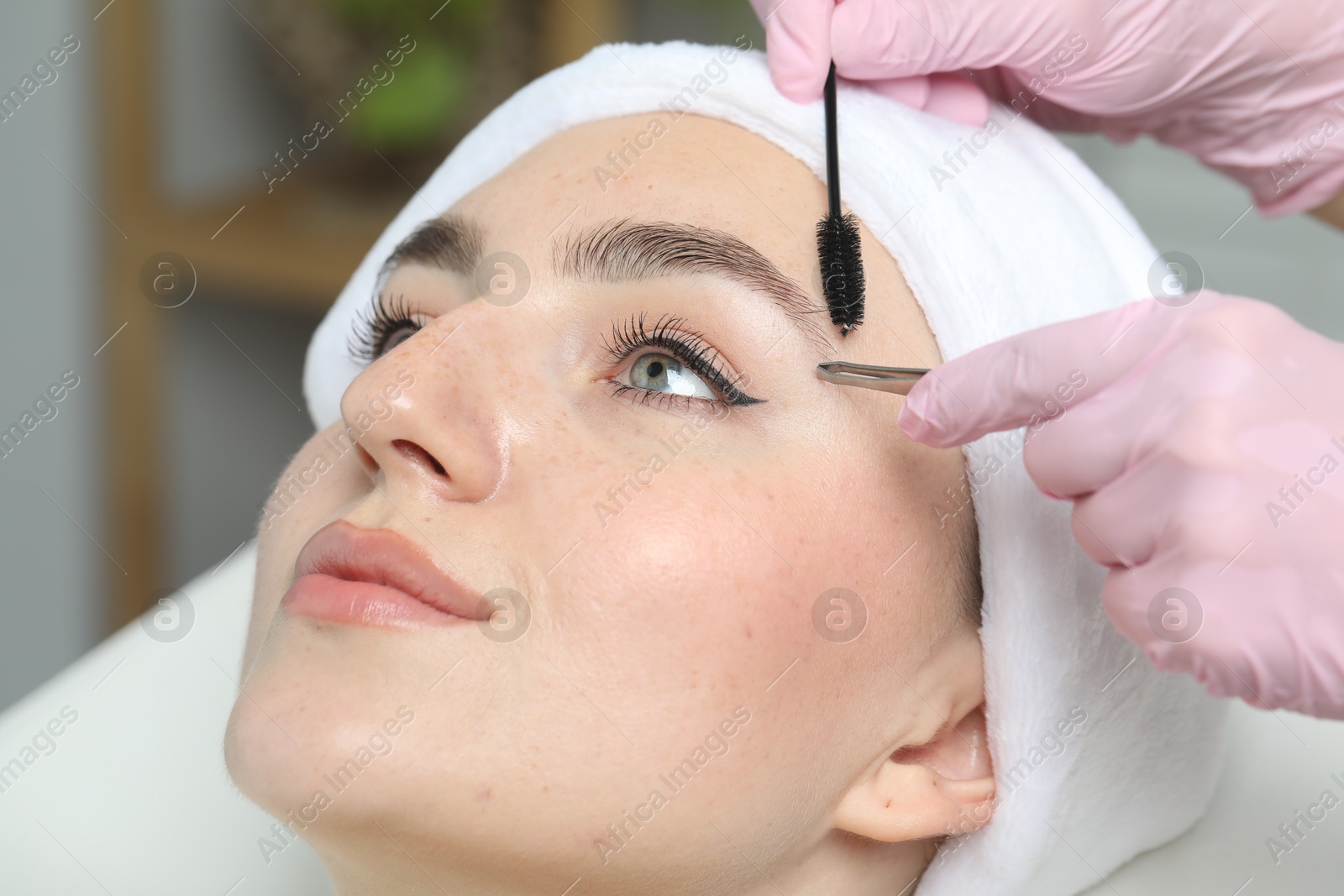 Photo of Beautician making eyebrow correction to young woman in beauty salon, closeup