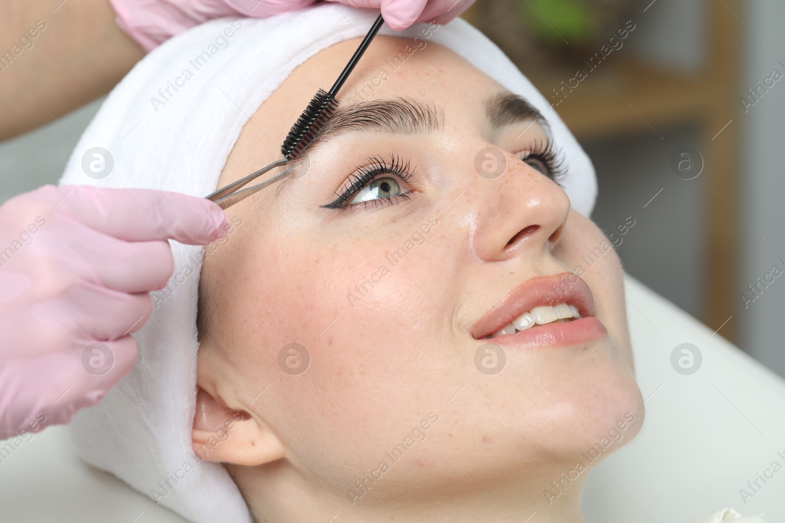 Photo of Beautician making eyebrow correction to young woman in beauty salon, closeup