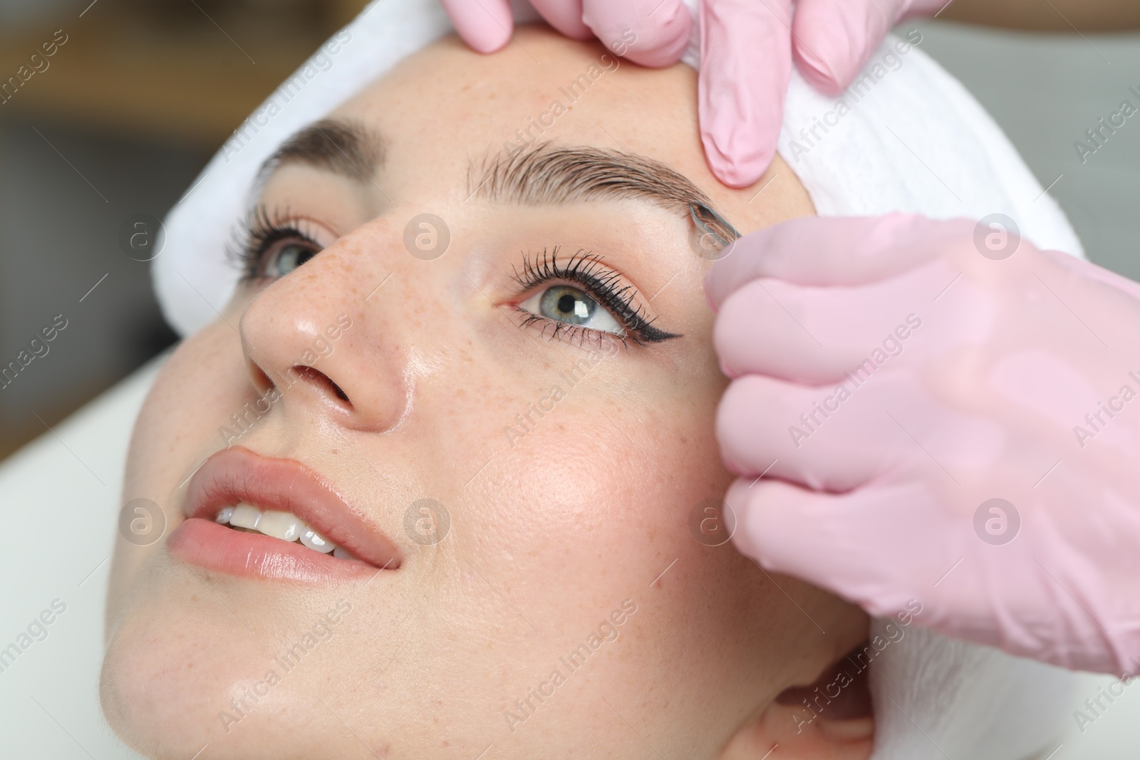 Photo of Beautician plucking young woman's eyebrow in beauty salon, closeup