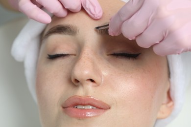 Photo of Beautician plucking young woman's eyebrow in beauty salon, closeup