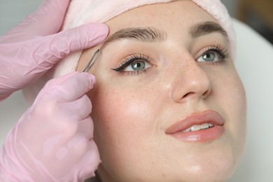Beautician plucking young woman's eyebrow in beauty salon, closeup