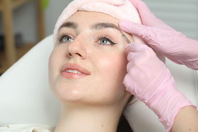 Photo of Beautician plucking young woman's eyebrow in beauty salon, closeup