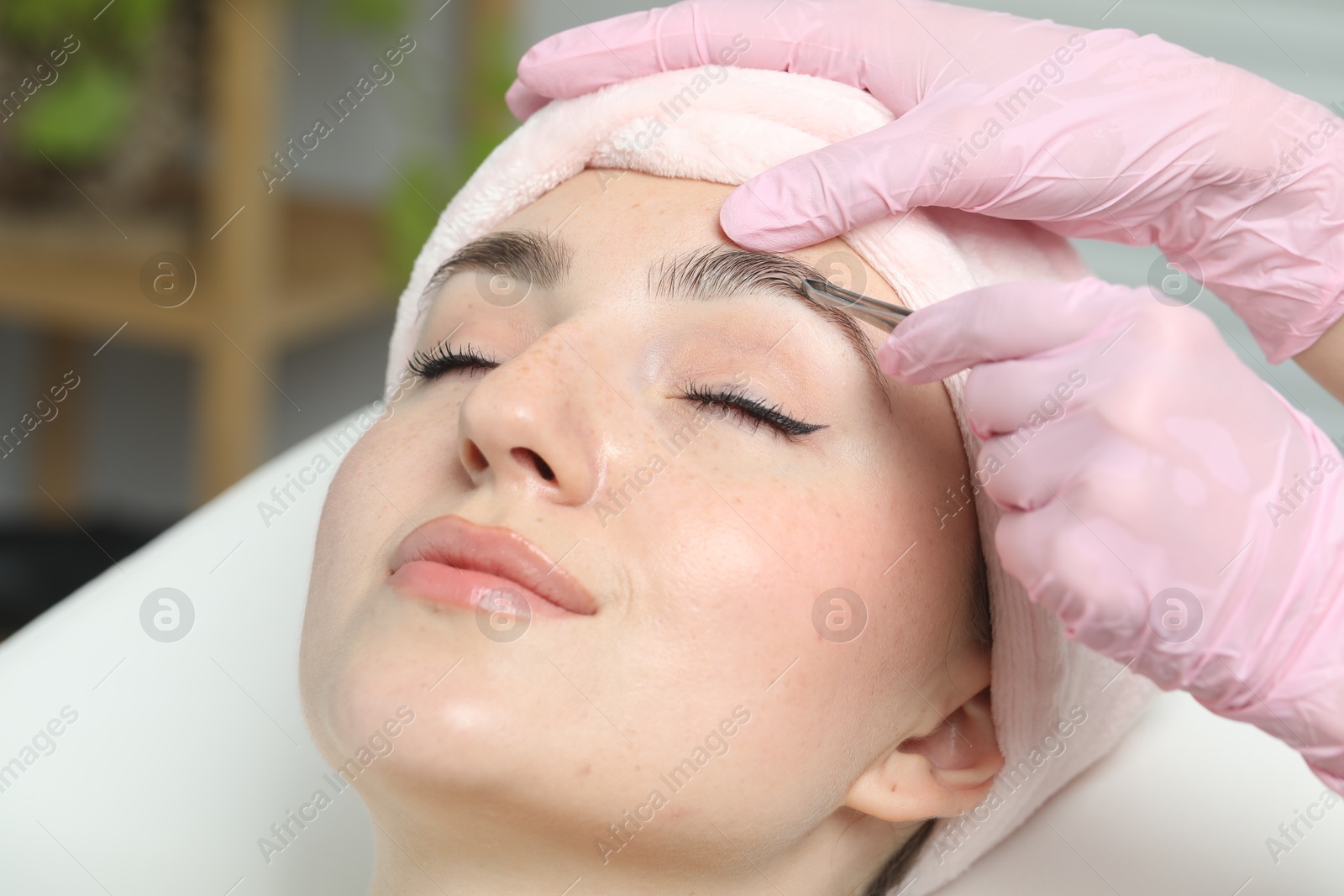 Photo of Beautician plucking young woman's eyebrow in beauty salon, closeup