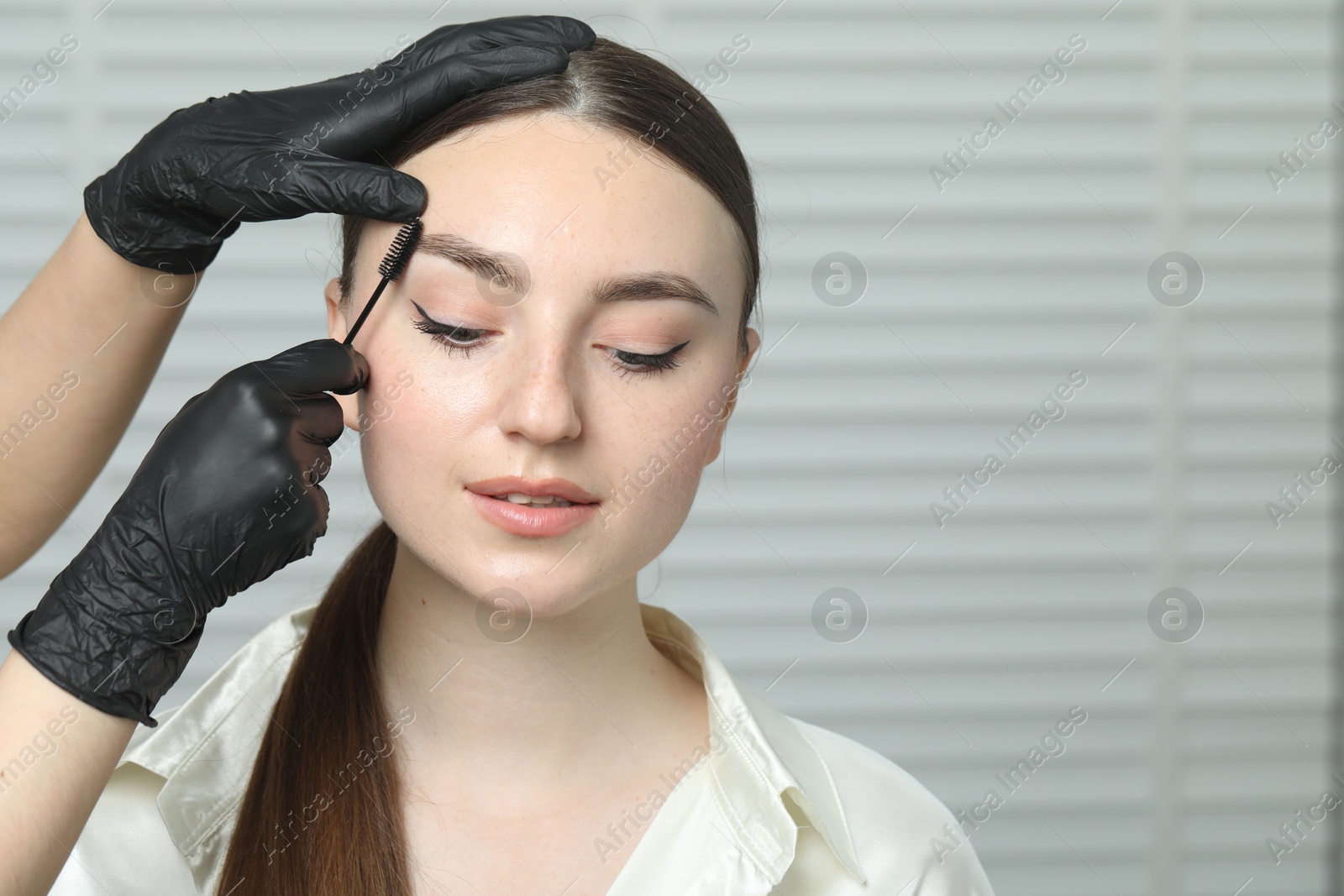 Photo of Beautician brushing young woman's eyebrow in beauty salon, closeup. Space for text