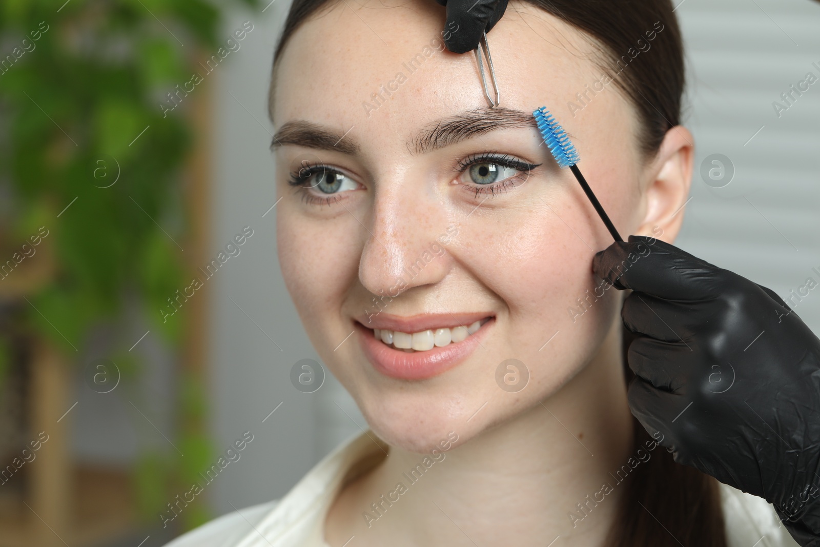 Photo of Beautician making eyebrow correction to young woman in beauty salon, closeup