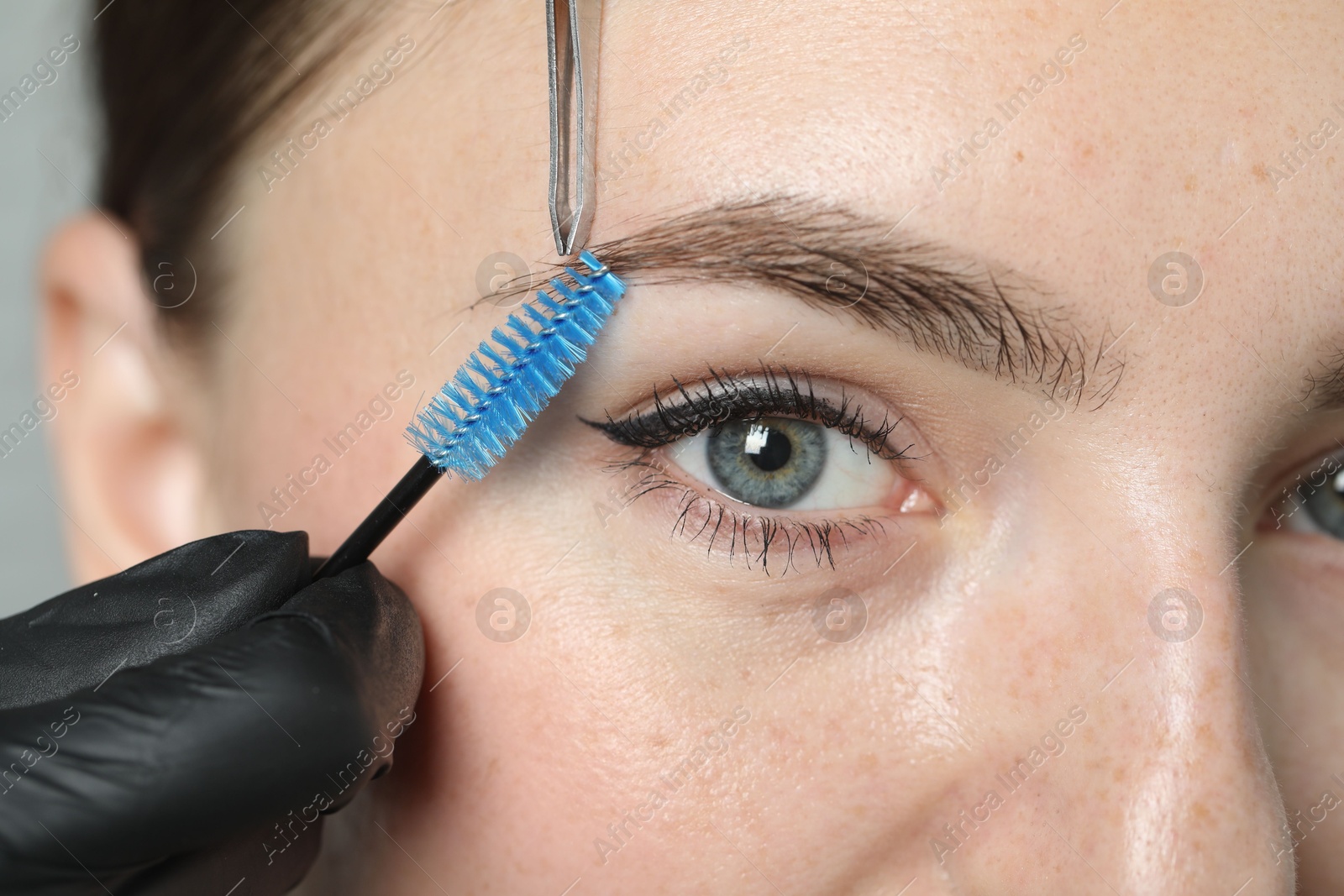 Photo of Beautician making eyebrow correction to young woman in beauty salon, closeup