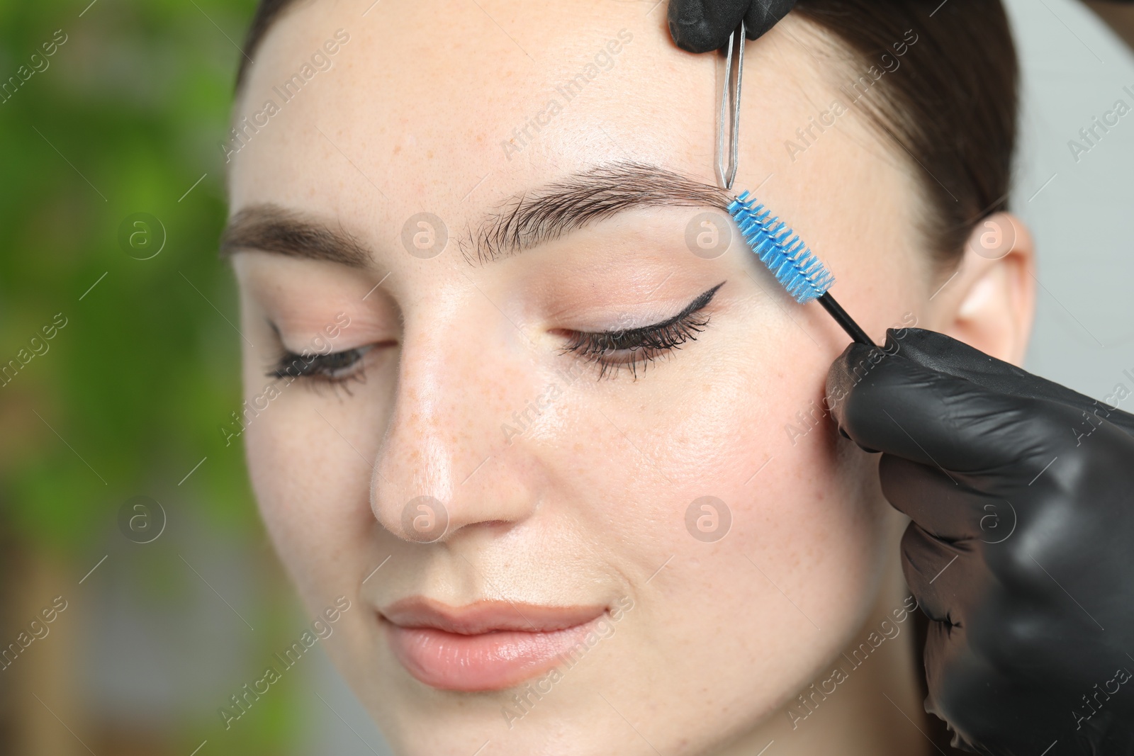 Photo of Beautician making eyebrow correction to young woman in beauty salon, closeup