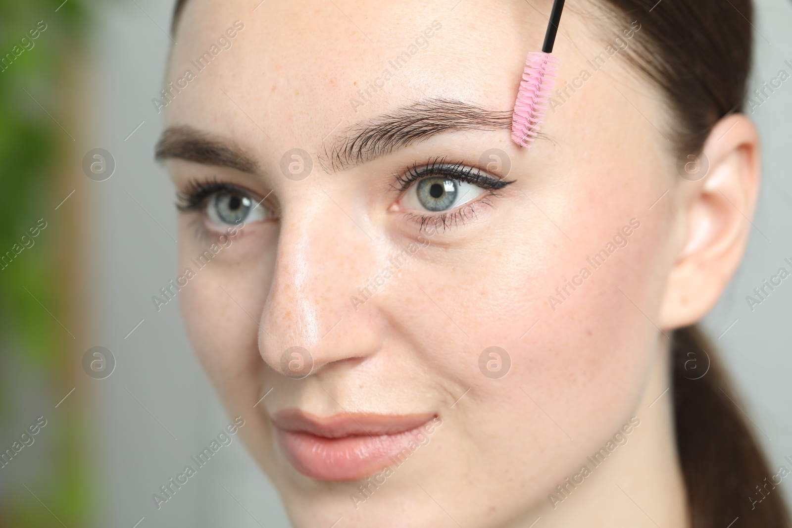 Photo of Woman brushing eyebrow on light background, closeup