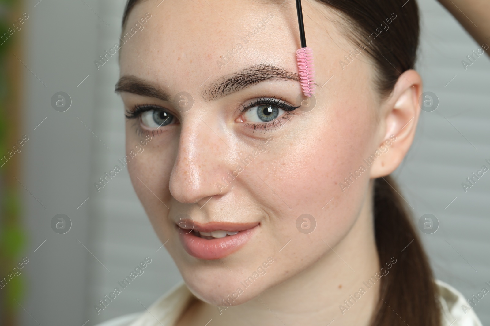 Photo of Beautician brushing young woman's eyebrow in beauty salon, closeup