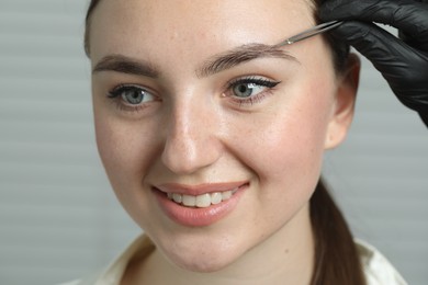 Photo of Beautician plucking young woman's eyebrow on light background, closeup