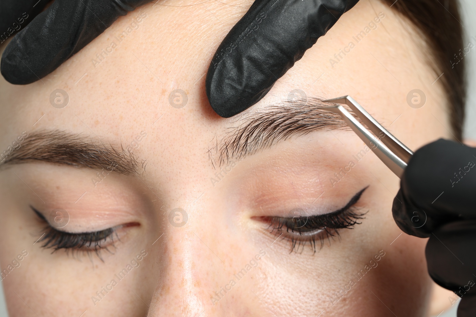 Photo of Beautician plucking young woman's eyebrow, closeup view