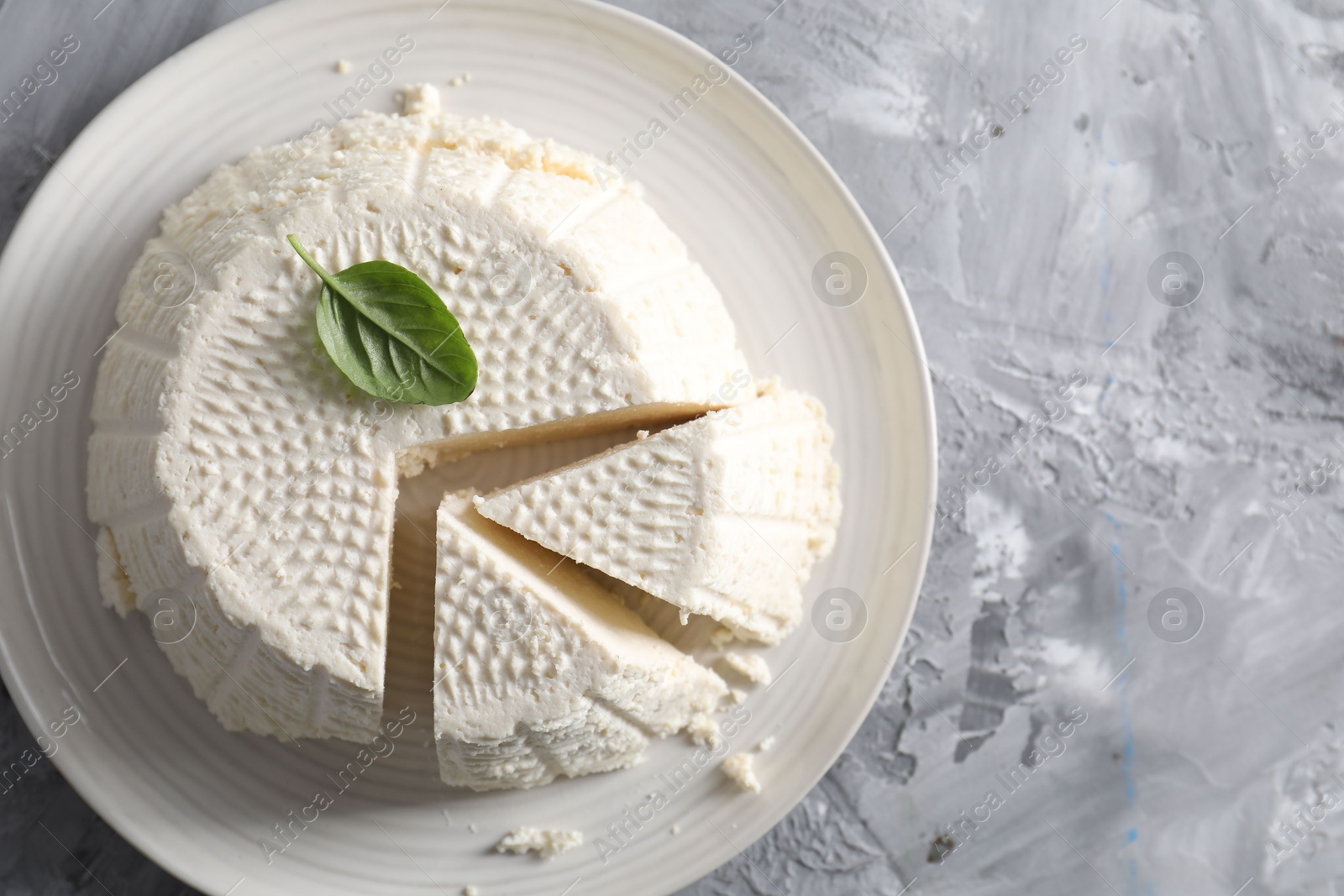 Photo of Tasty ricotta (cream cheese) on grey textured table, top view. Space for text