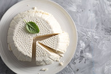 Photo of Tasty ricotta (cream cheese) on grey textured table, top view. Space for text