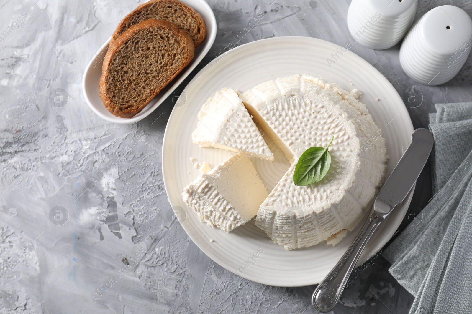 Photo of Tasty ricotta (cream cheese), bread and knife on grey table, flat lay