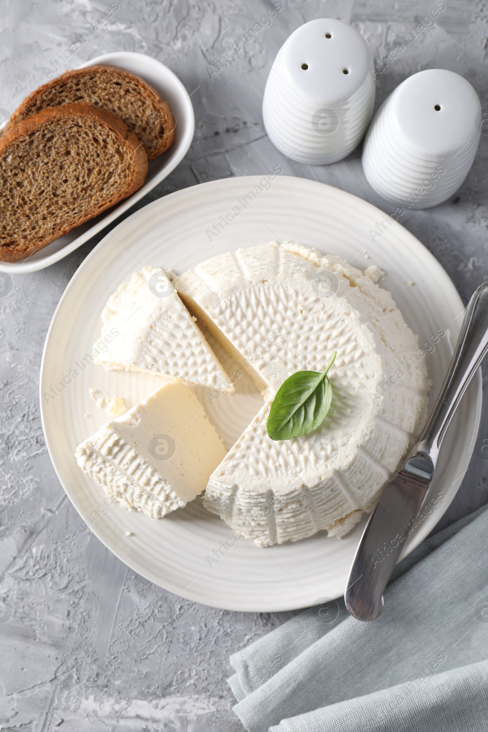 Photo of Tasty ricotta (cream cheese), bread and knife on grey table, flat lay