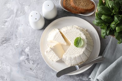 Tasty ricotta (cream cheese), bread, basil and knife on grey table, flat lay. Space for text