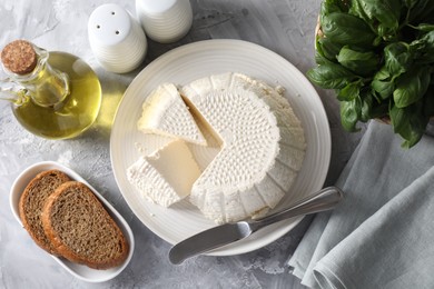 Tasty ricotta (cream cheese), bread, basil and knife on grey table, flat lay