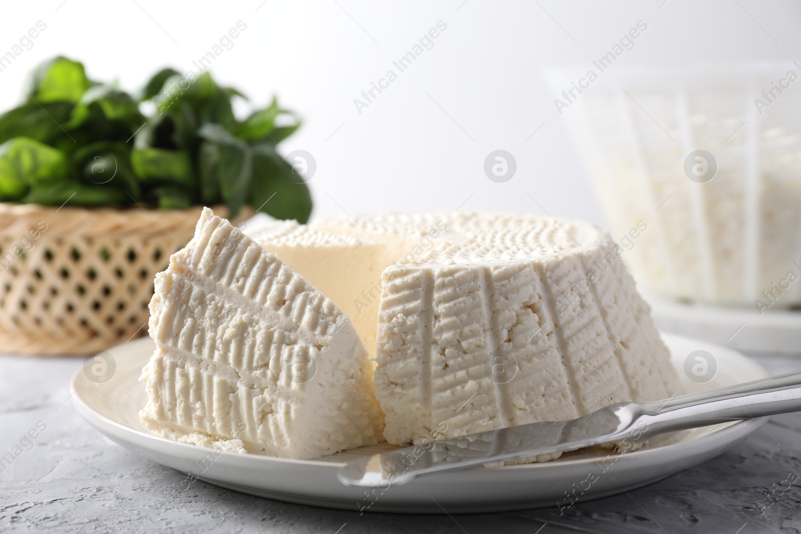 Photo of Tasty ricotta (cream cheese) and knife on grey textured table, closeup