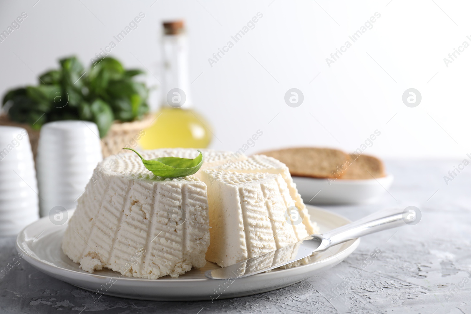 Photo of Tasty ricotta (cream cheese) and knife on grey textured table, closeup. Space for text