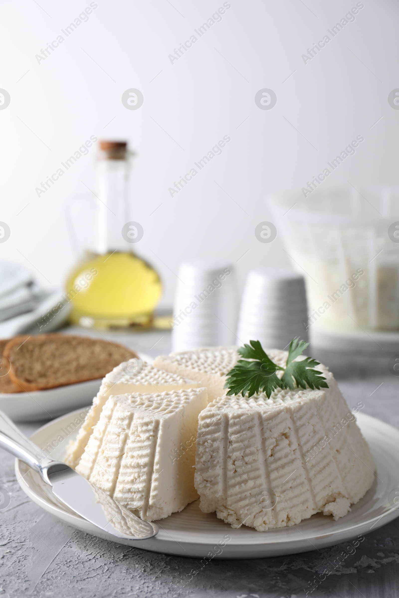 Photo of Tasty ricotta (cream cheese) and knife on grey textured table, closeup