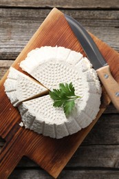 Photo of Tasty ricotta (cream cheese) and knife on wooden table, top view