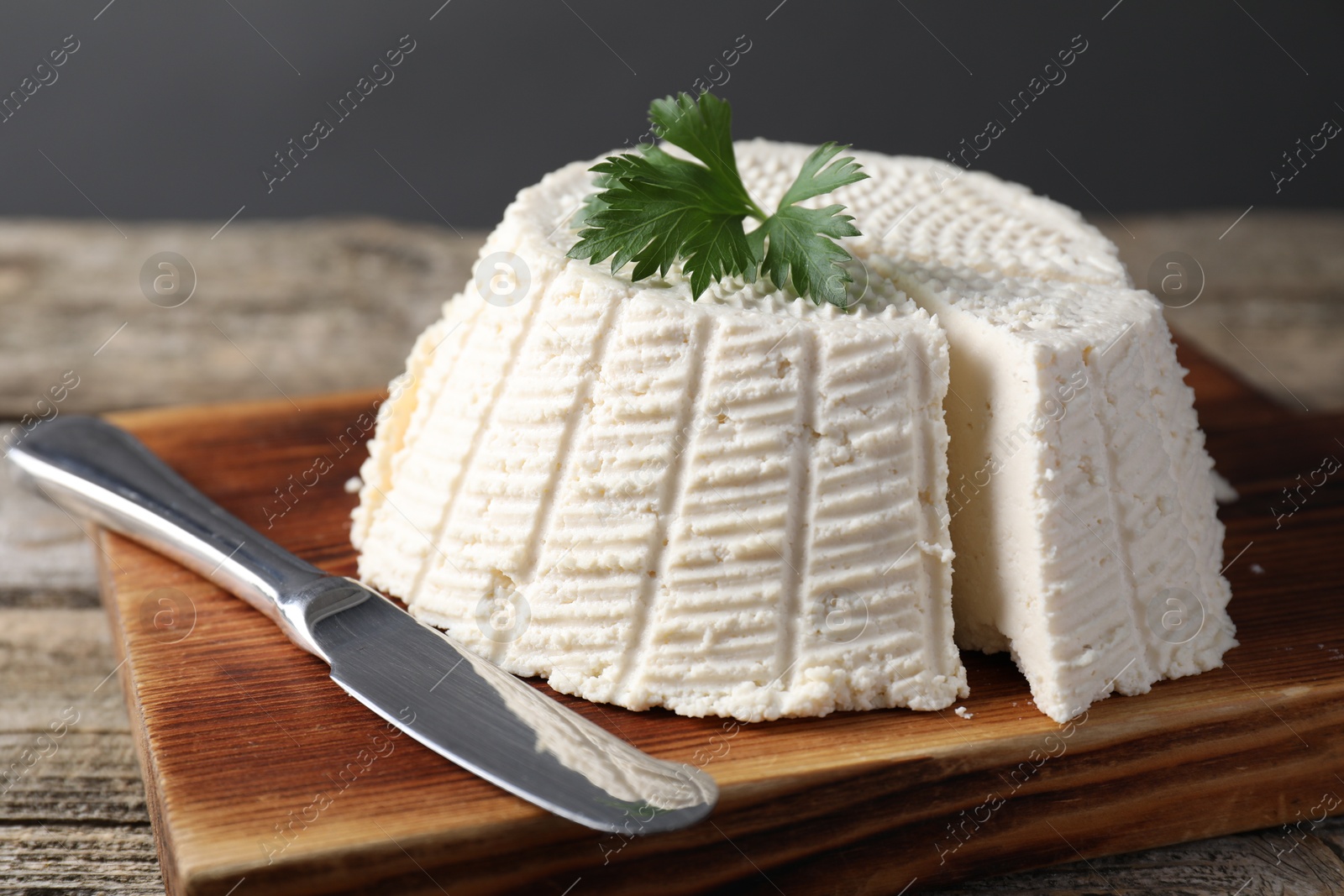 Photo of Tasty ricotta (cream cheese) and knife on wooden table, closeup