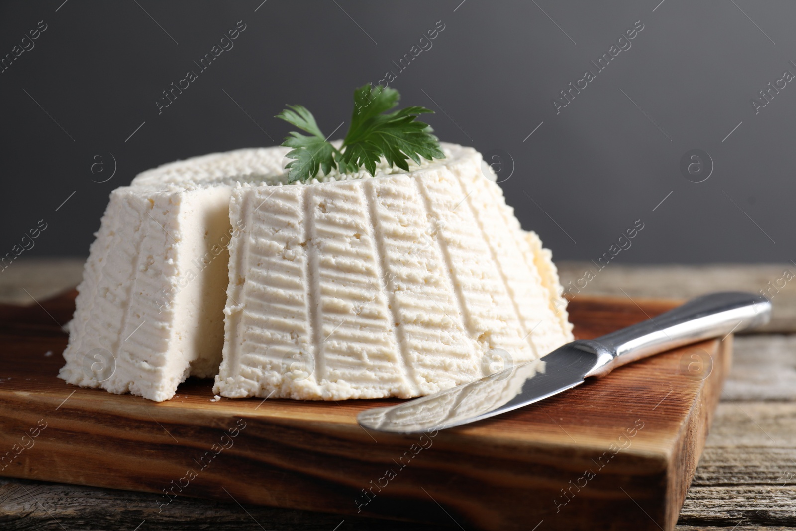 Photo of Tasty ricotta (cream cheese) and knife on wooden table, closeup