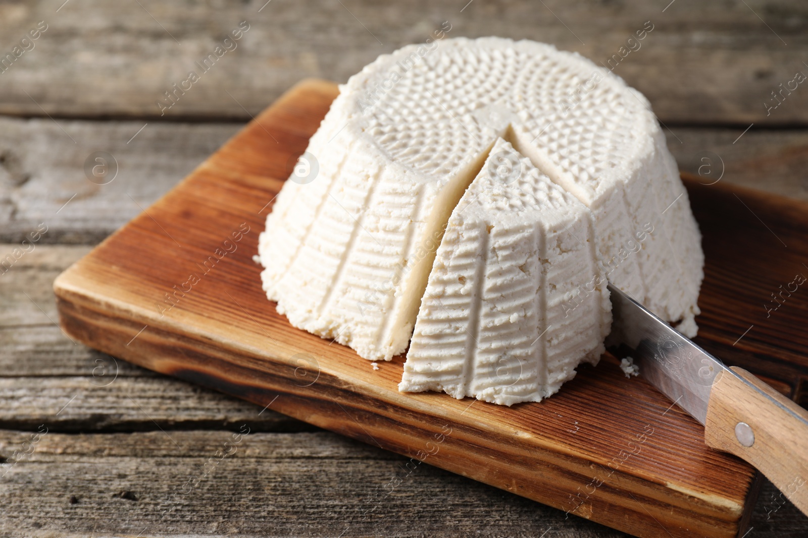 Photo of Tasty ricotta (cream cheese) and knife on wooden table, closeup