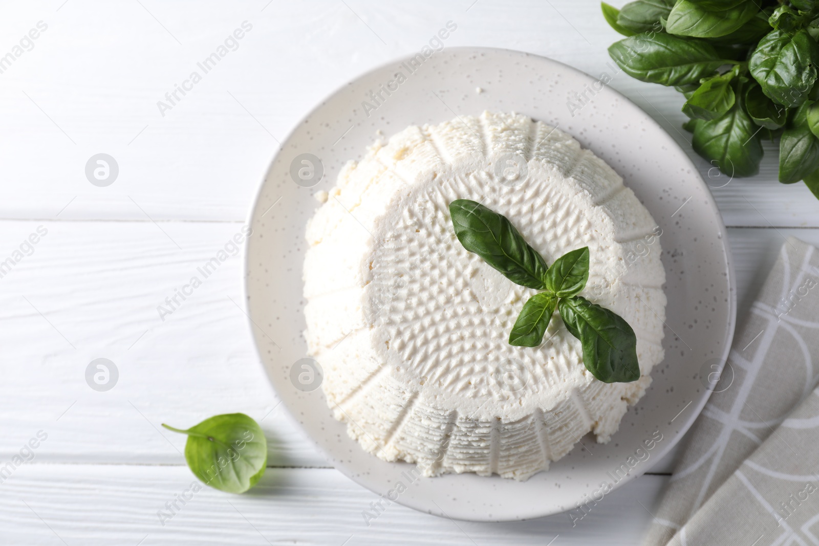 Photo of Tasty ricotta (cream cheese) and basil on white wooden table, flat lay. Space for text