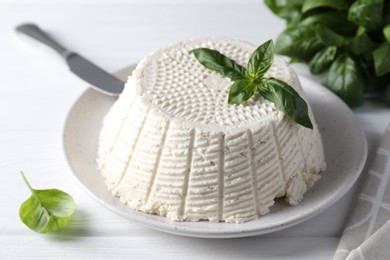 Tasty ricotta (cream cheese), knife and basil on white wooden table, closeup