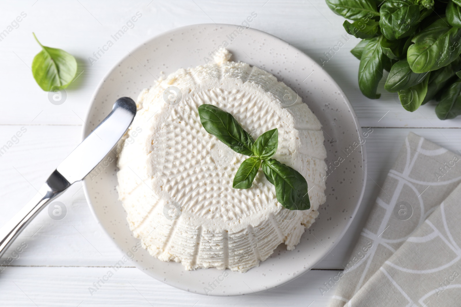 Photo of Tasty ricotta (cream cheese), knife and basil on white wooden table, top view