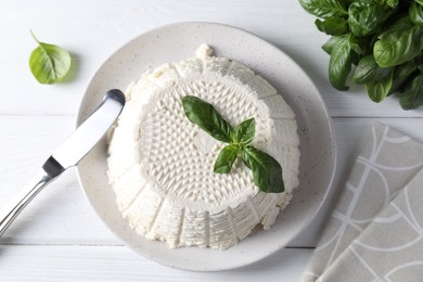 Photo of Tasty ricotta (cream cheese), knife and basil on white wooden table, top view