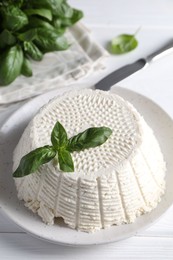 Photo of Tasty ricotta (cream cheese), knife and basil on white wooden table, closeup