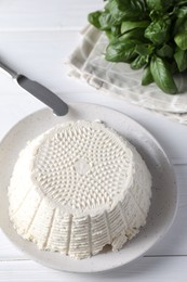 Photo of Tasty ricotta (cream cheese), knife and basil on white wooden table