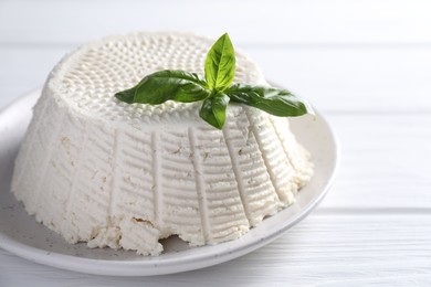 Photo of Tasty ricotta (cream cheese) and basil on white wooden table, closeup