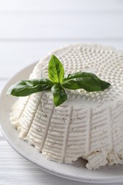 Photo of Tasty ricotta (cream cheese) and basil on white wooden table, closeup