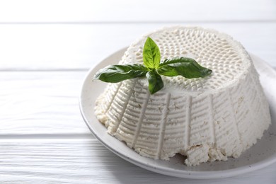 Tasty ricotta (cream cheese) and basil on white wooden table, closeup. Space for text