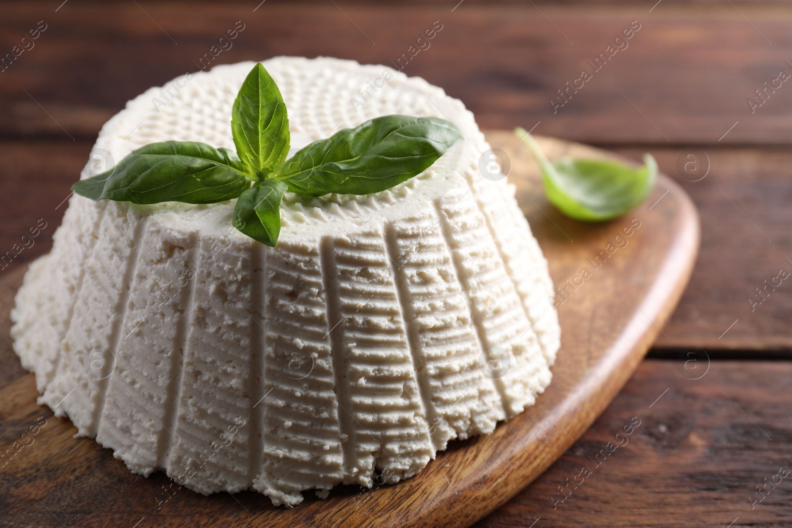 Photo of Tasty ricotta (cream cheese) and basil on wooden table, closeup