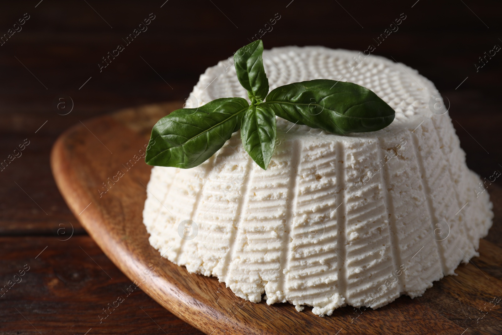 Photo of Tasty ricotta (cream cheese) and basil on wooden table, closeup