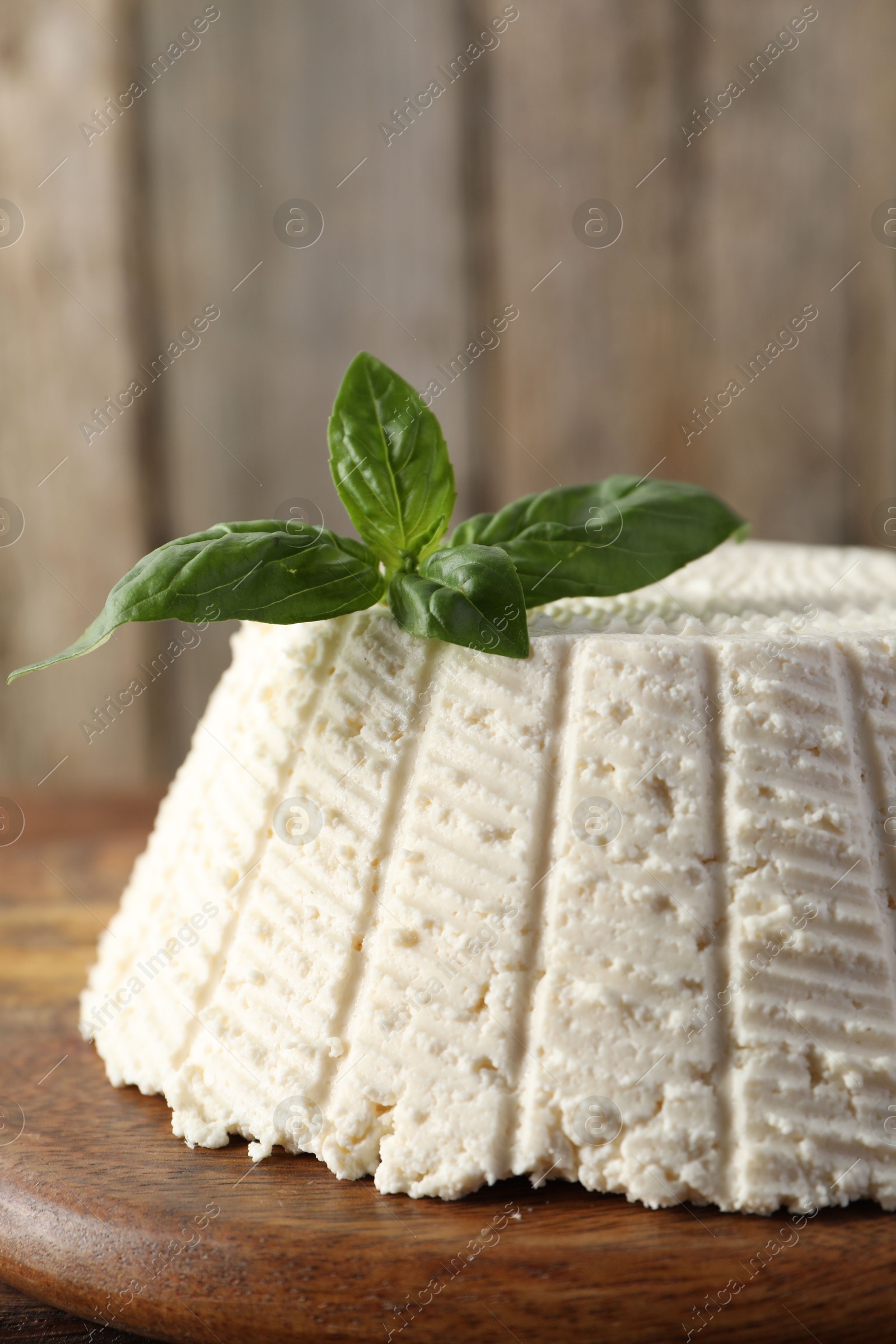 Photo of Tasty ricotta (cream cheese) and basil on wooden table, closeup