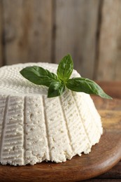 Photo of Tasty ricotta (cream cheese) and basil on wooden table, closeup