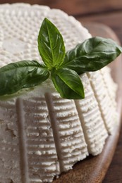 Tasty ricotta (cream cheese) and basil on wooden table, closeup