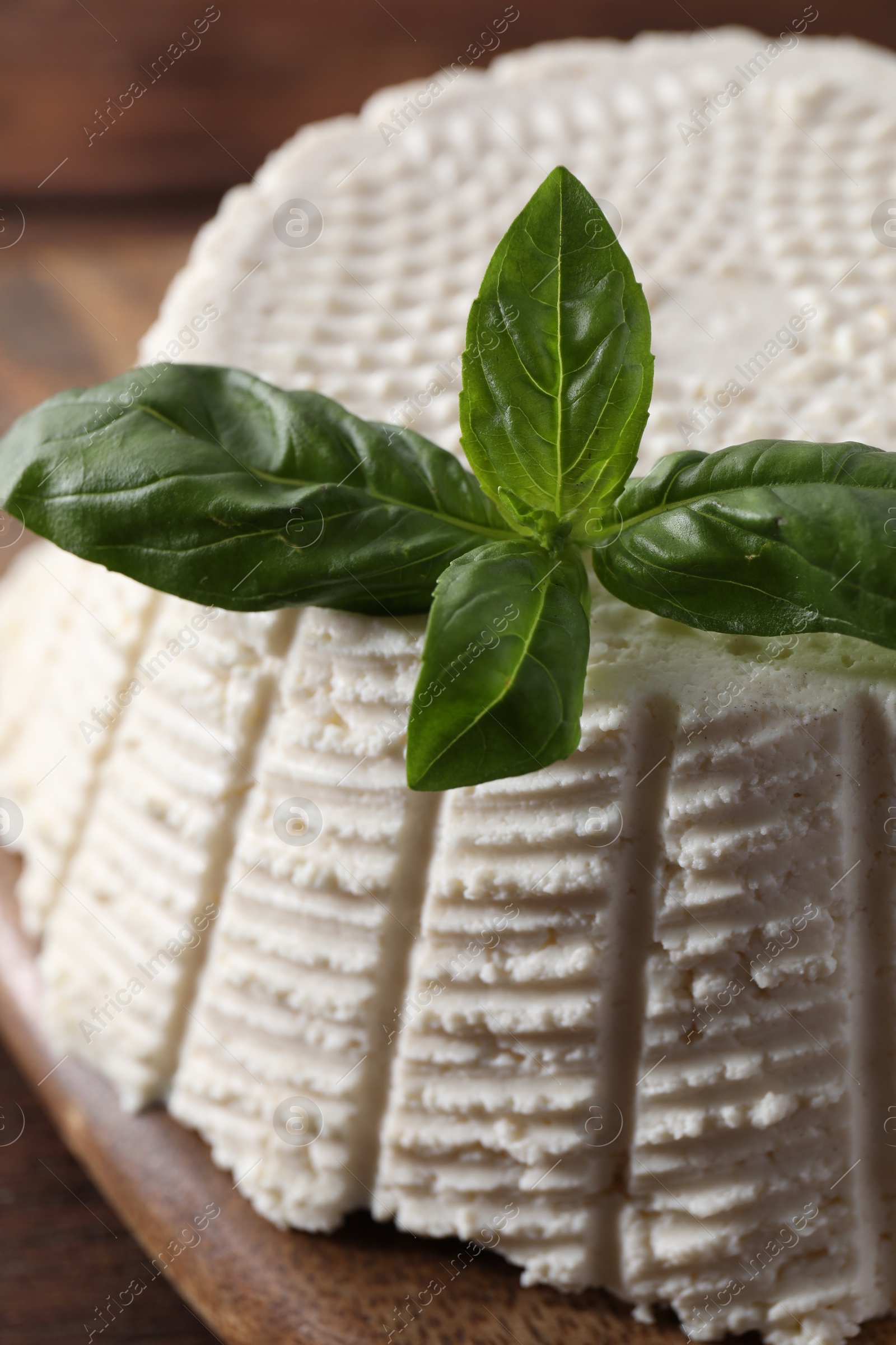 Photo of Tasty ricotta (cream cheese) and basil on wooden table, closeup