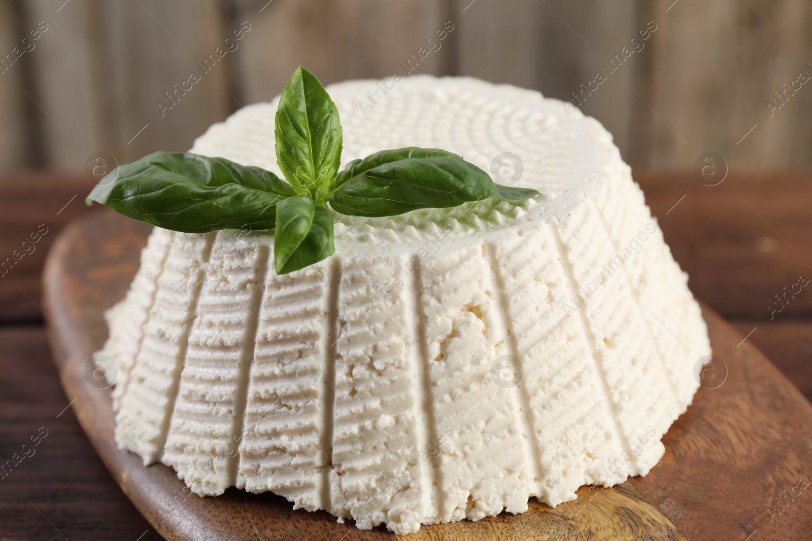 Photo of Tasty ricotta (cream cheese) and basil on wooden table, closeup