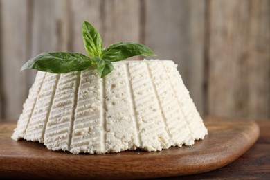 Photo of Tasty ricotta (cream cheese) and basil on wooden table, closeup