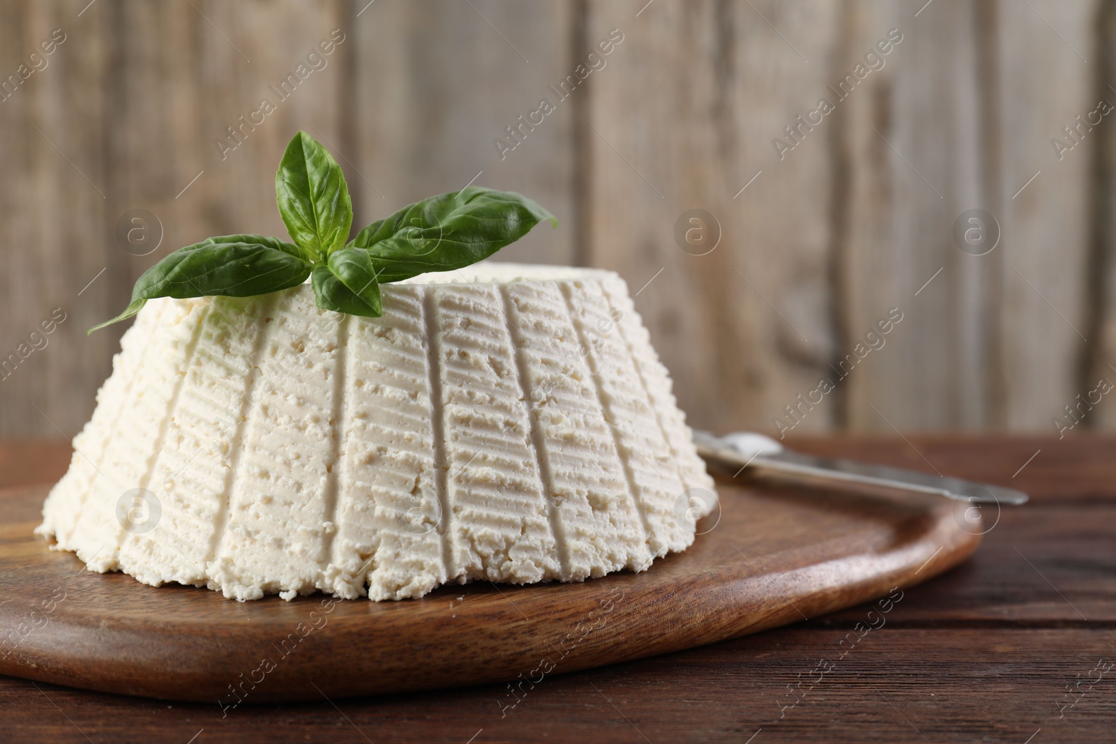 Photo of Tasty ricotta (cream cheese), basil and knife on wooden table, closeup