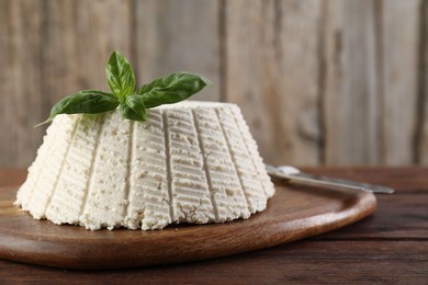 Tasty ricotta (cream cheese), basil and knife on wooden table, closeup