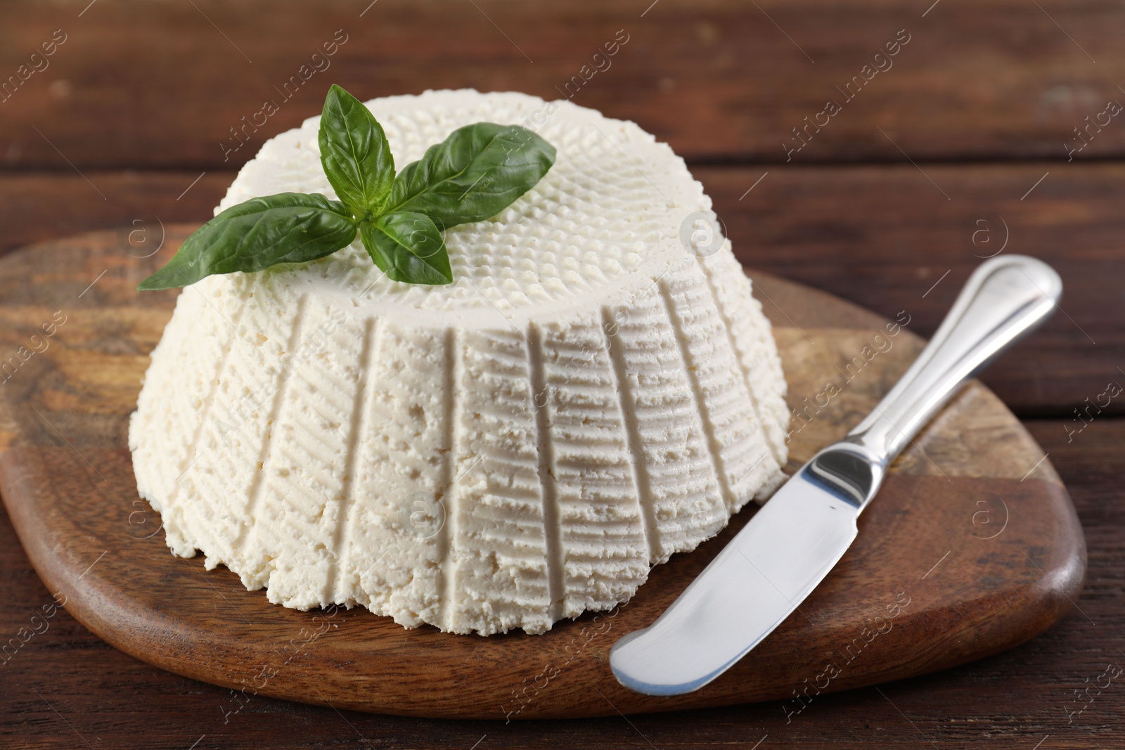 Photo of Tasty ricotta (cream cheese), basil and knife on wooden table, closeup