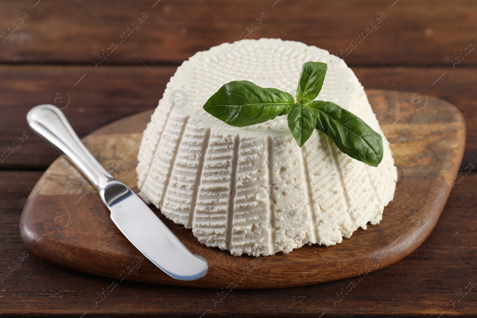 Photo of Tasty ricotta (cream cheese), basil and knife on wooden table, closeup