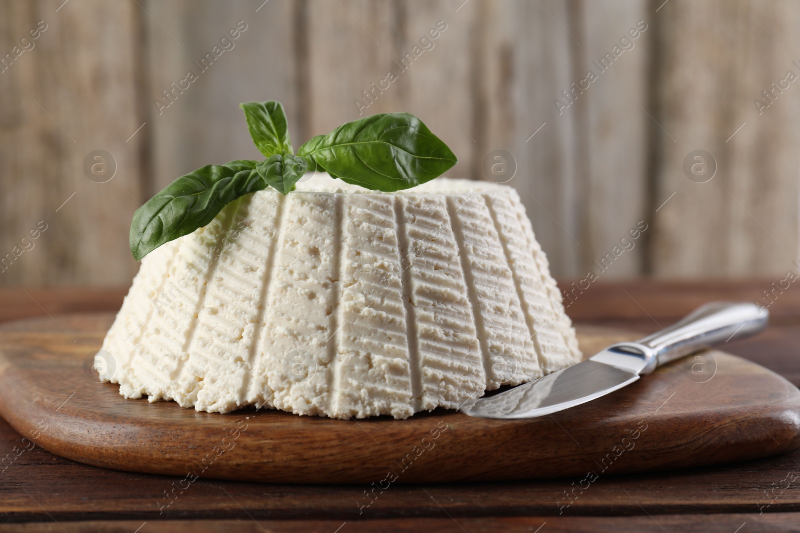 Photo of Tasty ricotta (cream cheese), basil and knife on wooden table, closeup